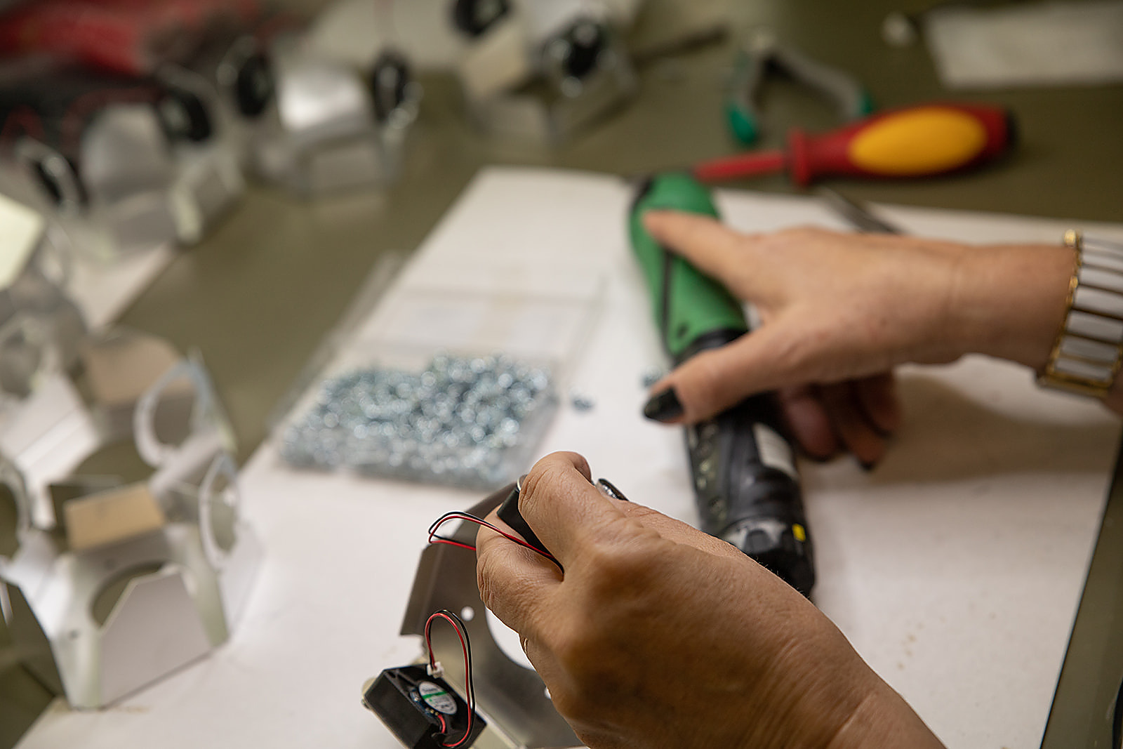 Hands-on engineering work at a Kii.am workbench: soldering iron, magnifier lamp, components
